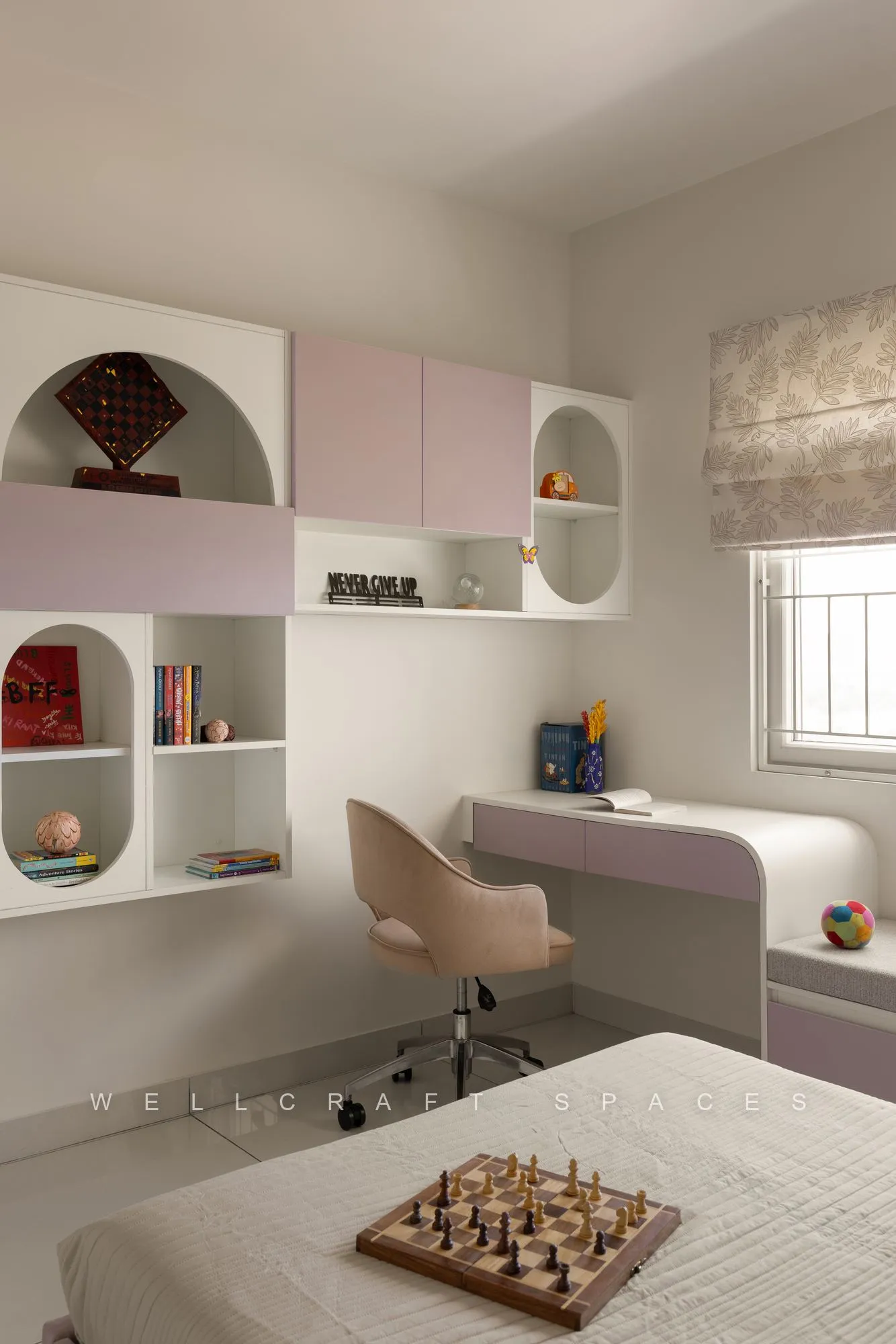 Study corner in the child's room with arched lilac and pink niches holding books and toys, a compact desk and a cream chair.