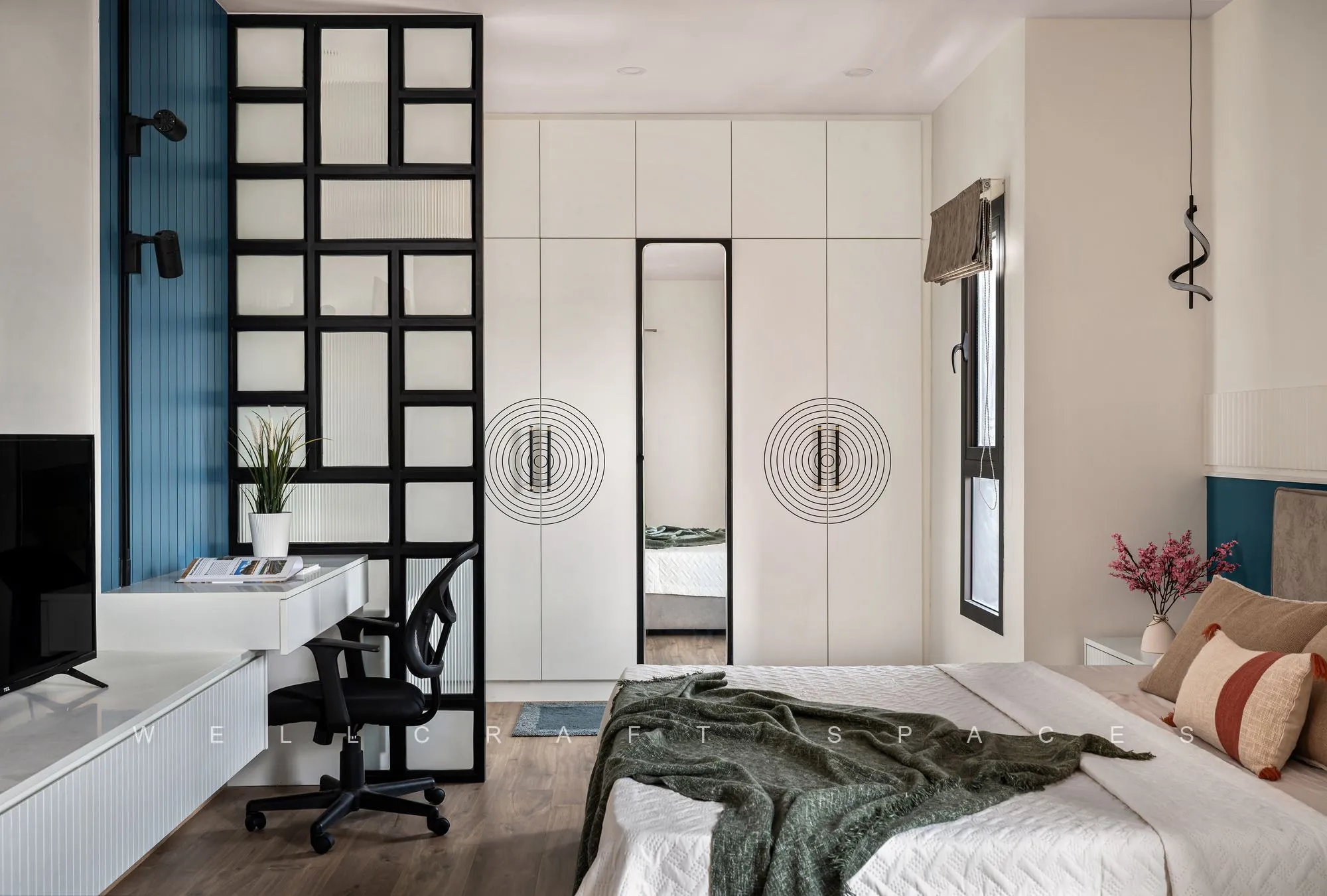 Bedroom wardrobe wall in white with circular ring pulls, a full-length mirror insert and a black-framed reeded-glass partition beside a blue accent wall.