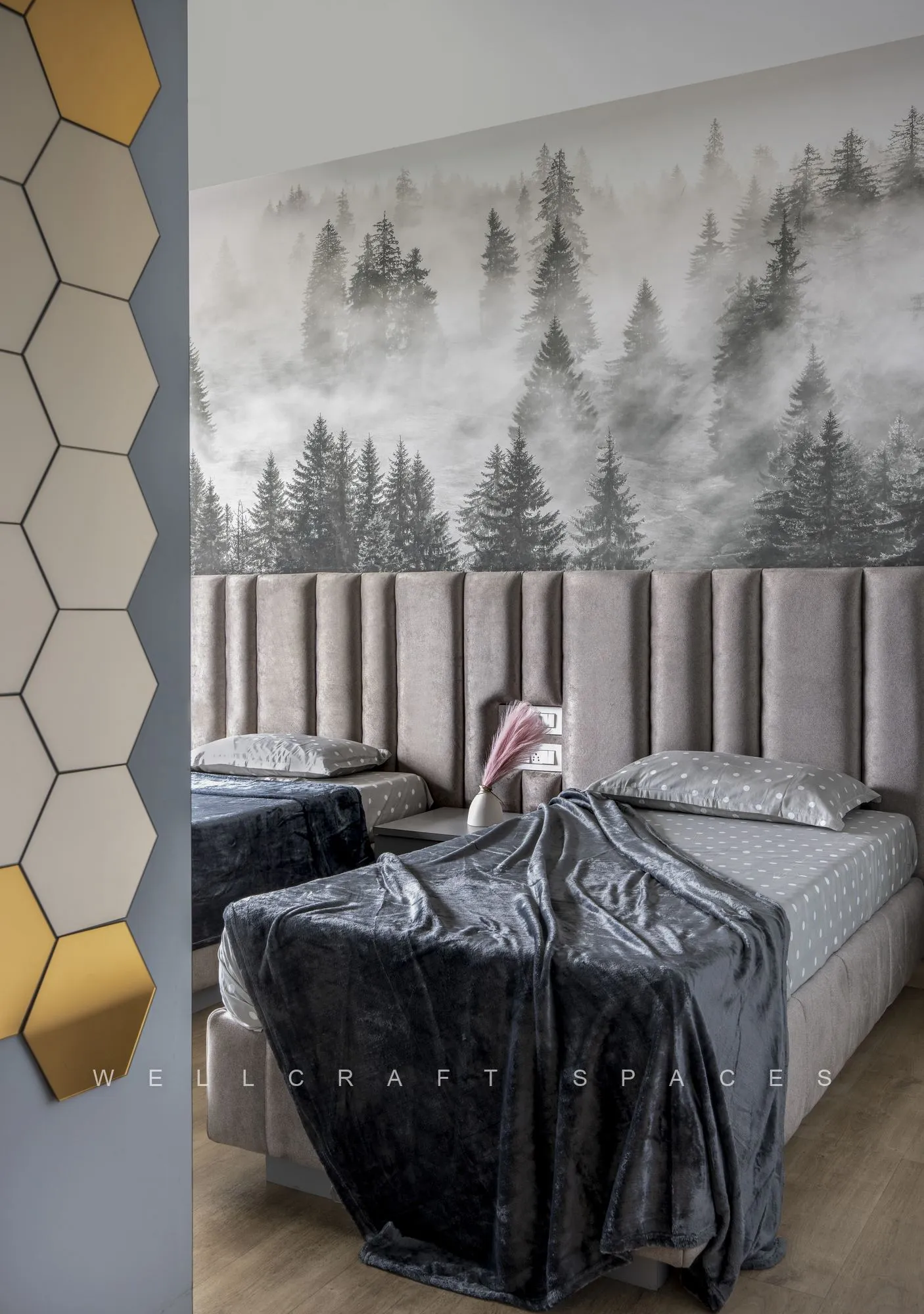 Twin bed against a misty forest mural with a grey channel-tufted headboard, velvet throw and a cluster of gold and mirrored hexagonal wall tiles.