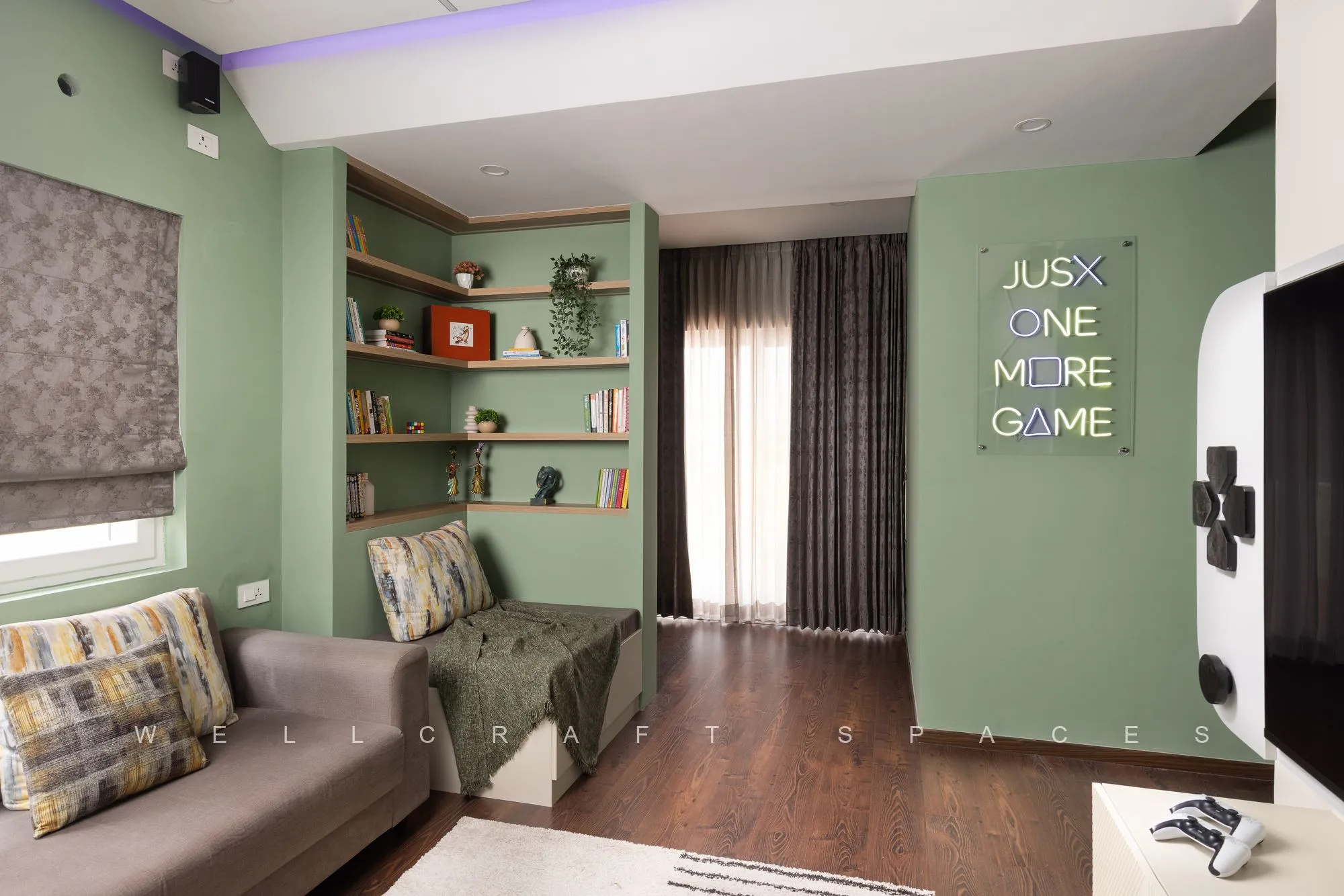 Games and media room in sage green with a low grey daybed, open timber shelves, blackout curtains and a large wall-mounted screen.