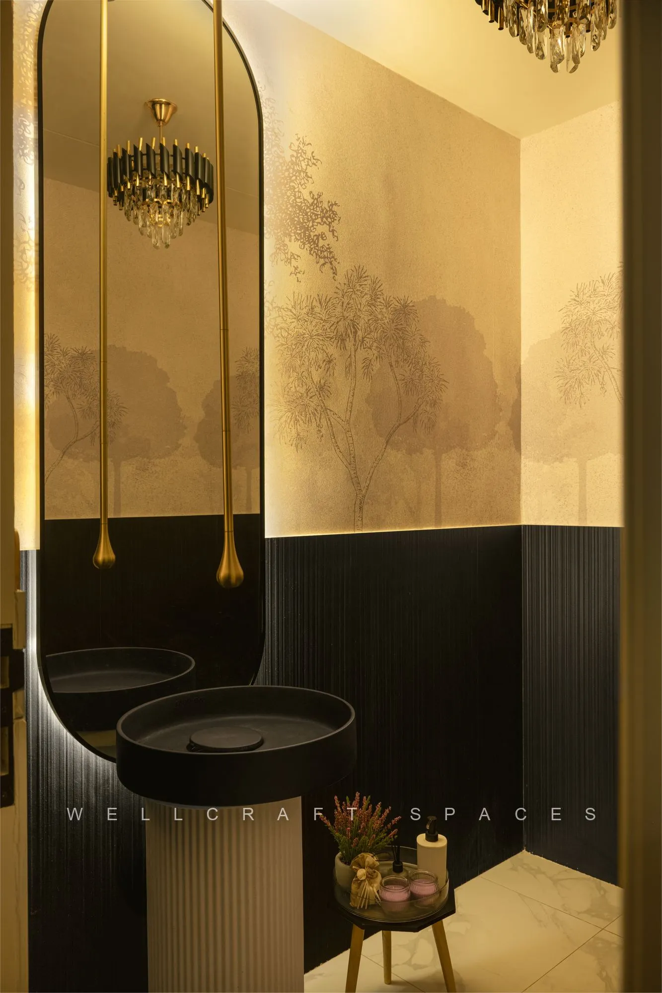 Powder room in gold leaf mural wallpaper over a black panelled dado, with a black vessel basin, round mirror and a slim brass pendant.