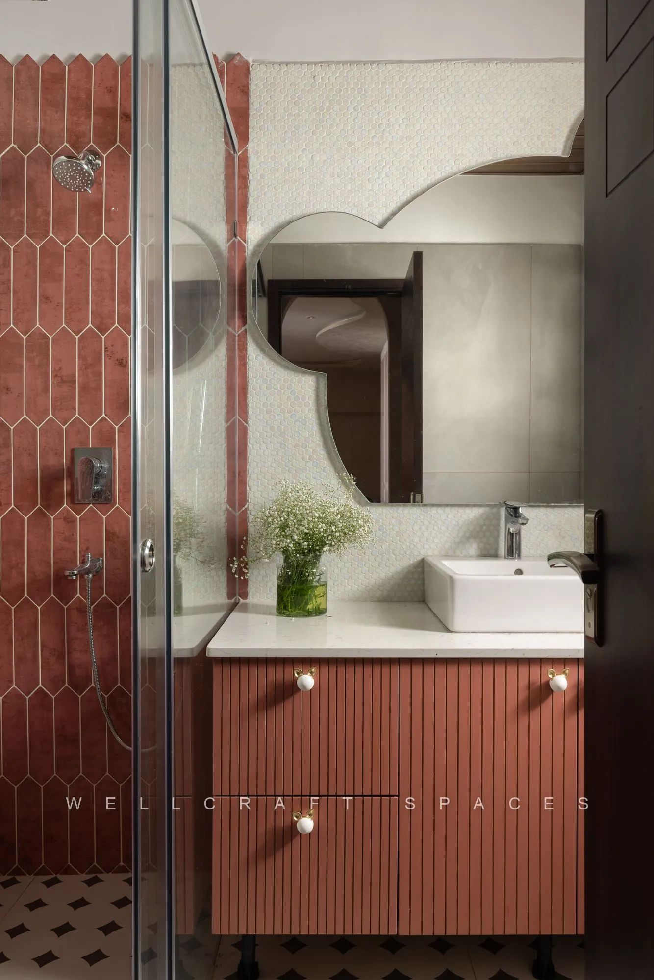 Bathroom in terracotta fluted tile with a rust vanity, white vessel basin, sculpted mirror and a glass shower screen.
