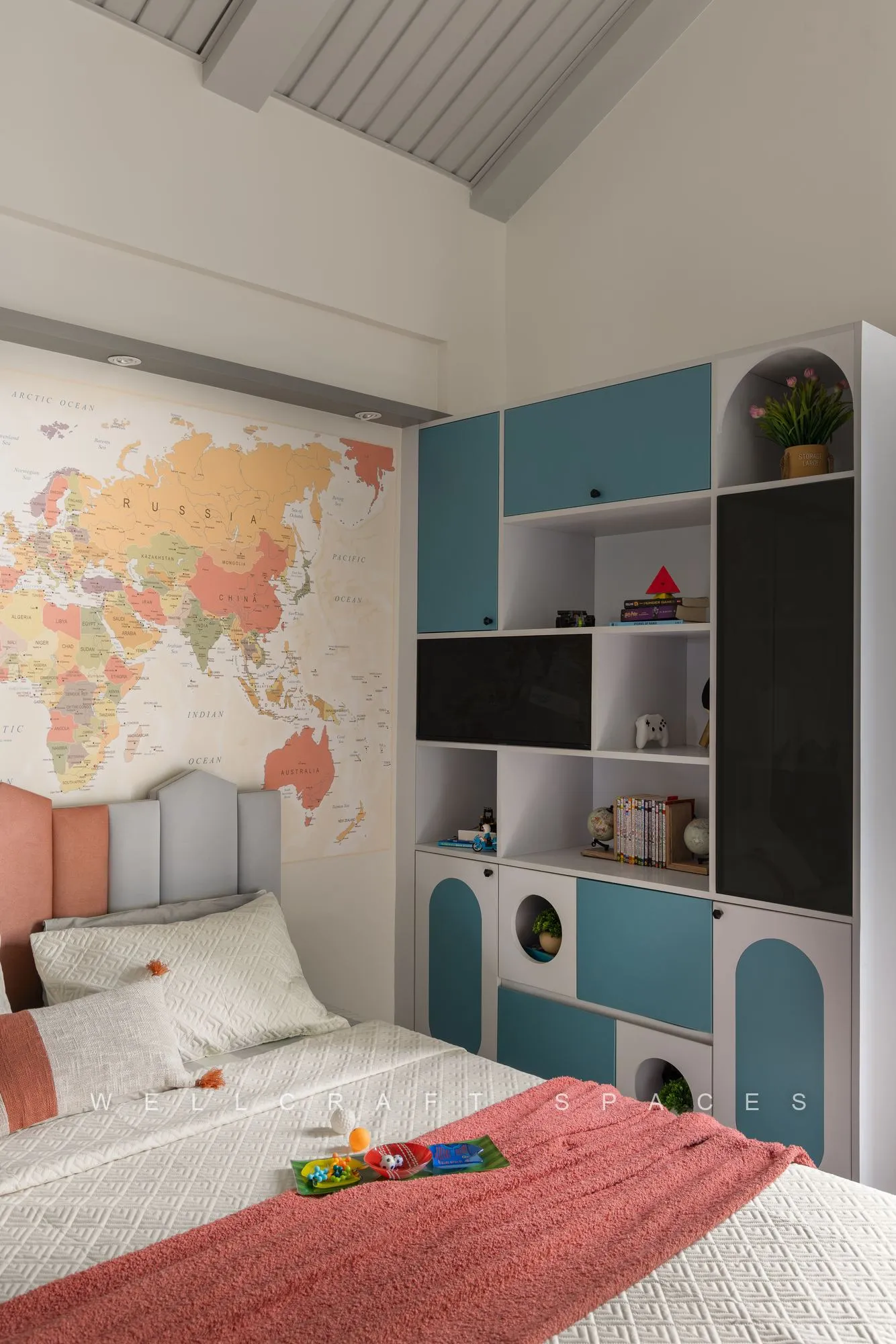 Kids room with a world map mural, blue and white storage shelving around the television and a coral bedspread.