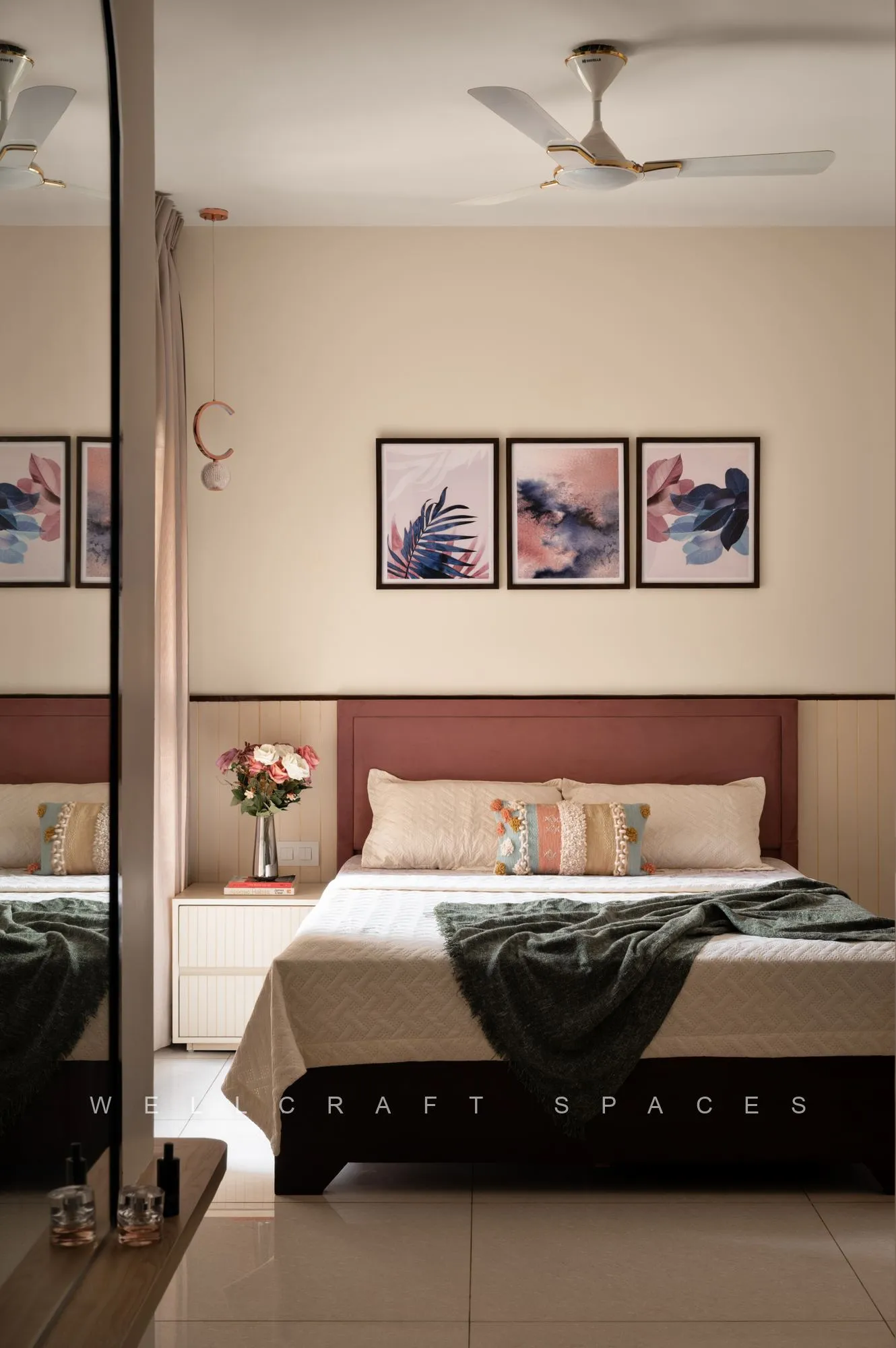 Guest bedroom with a rust upholstered headboard, framed botanical triptych, grey throw and a mirrored wardrobe reflecting the room.