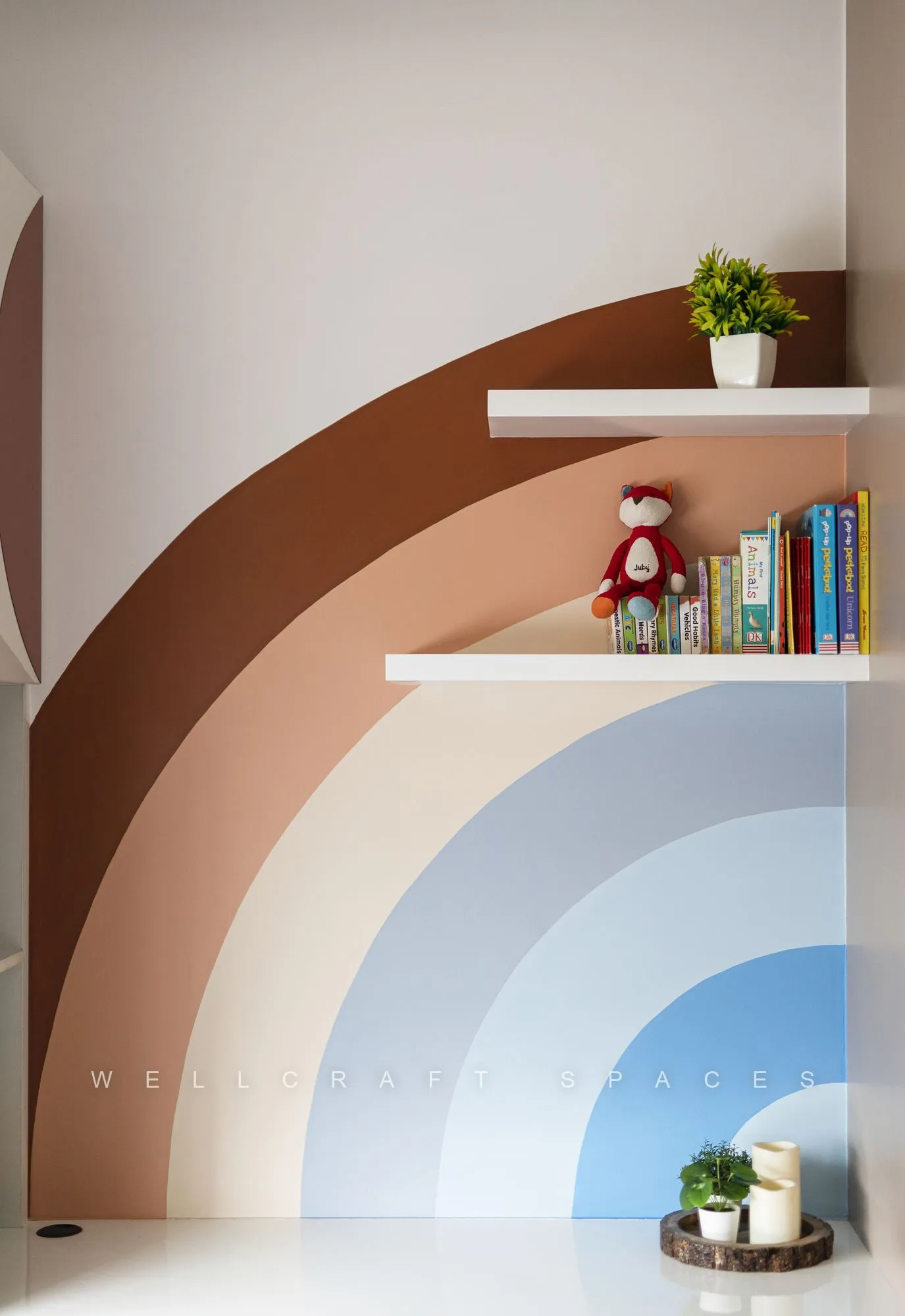 Close view of the rainbow arch motif in terracotta, pink and blue, with floating white shelves holding books and a plant.