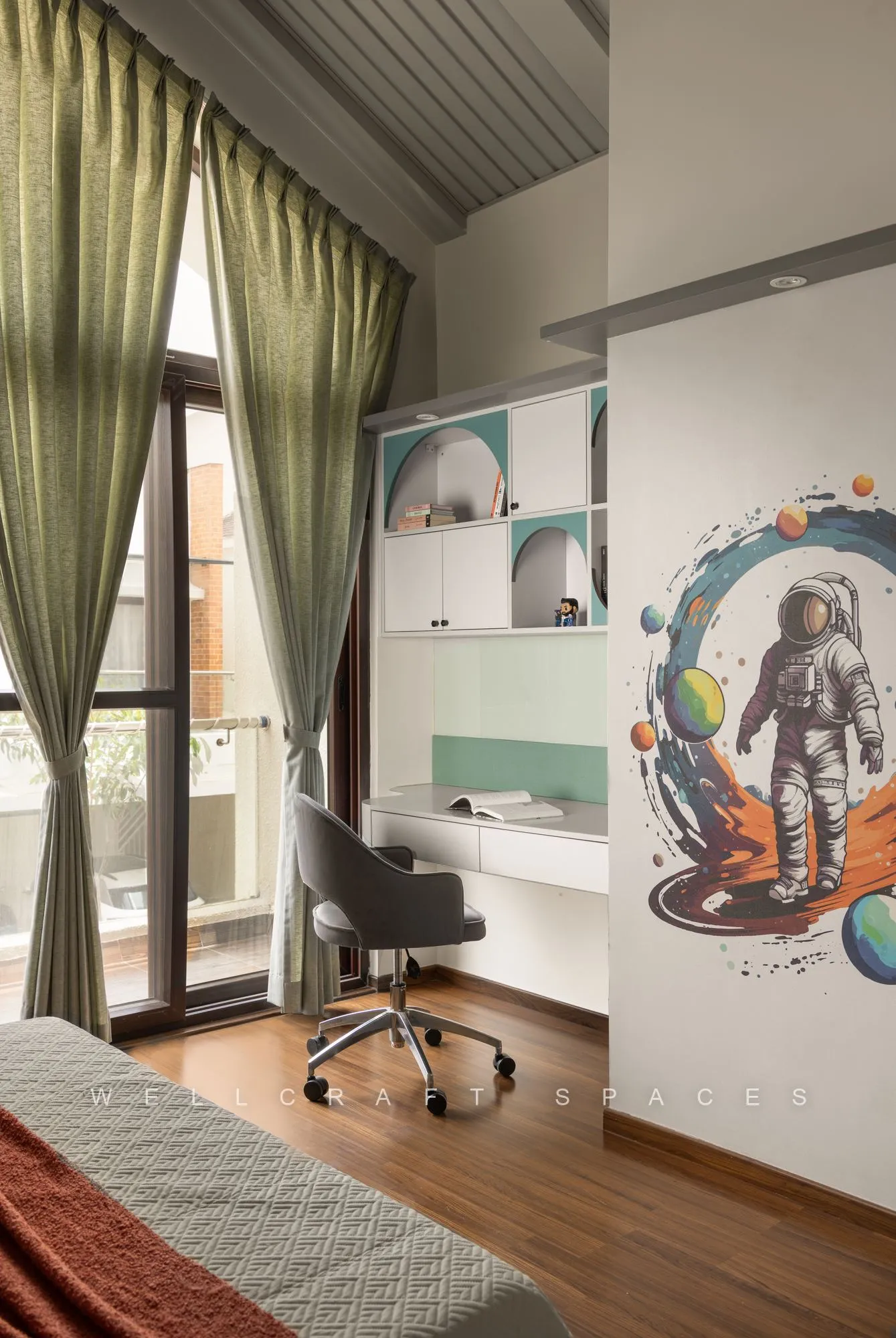 Kids study zone beside a balcony door with olive curtains, an astronaut wall mural, floating mint shelves and a grey desk chair.
