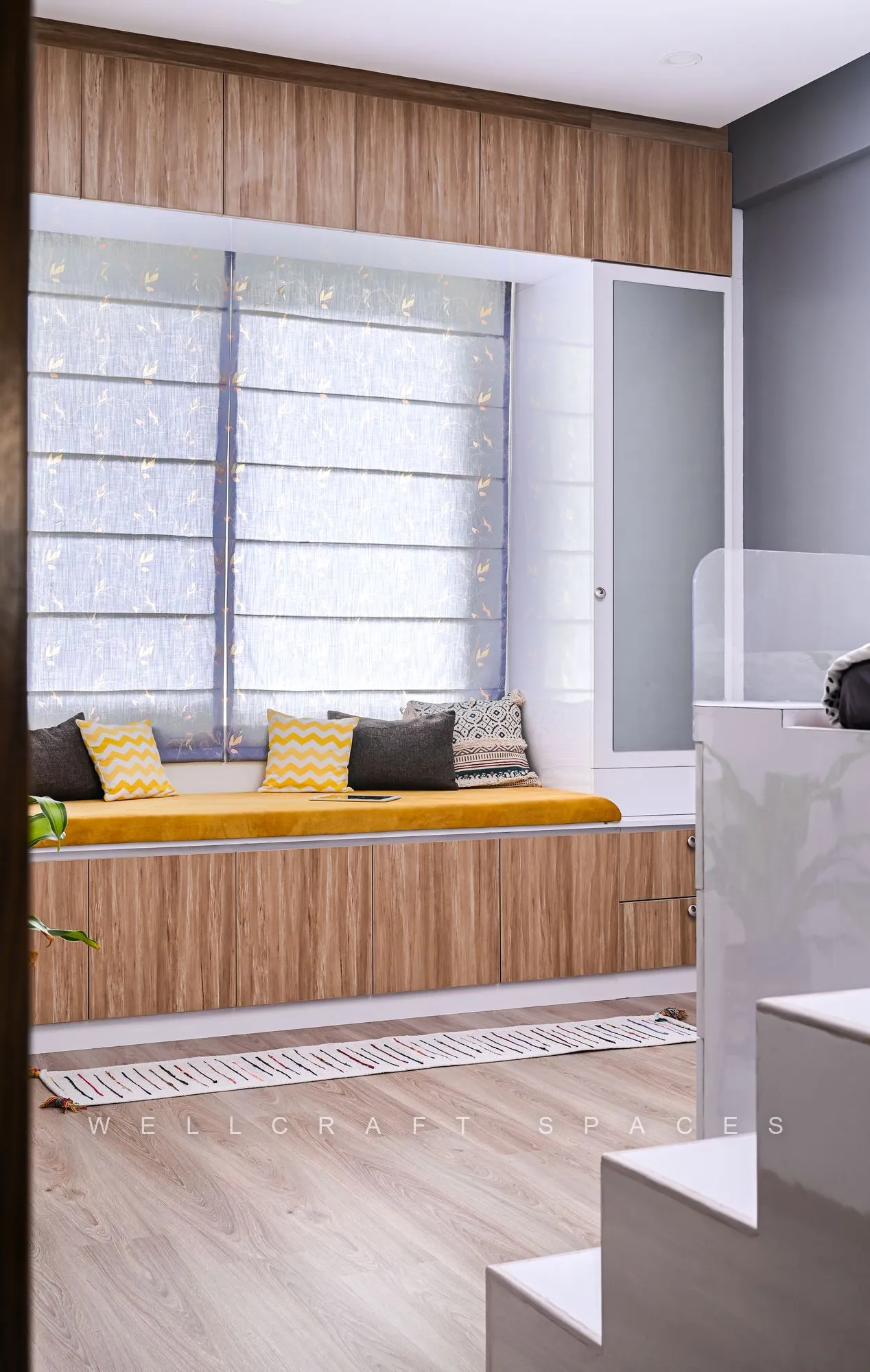 Window seat in timber with mustard cushions beside a frosted glass wall and a stepped white side unit on pale wood flooring.