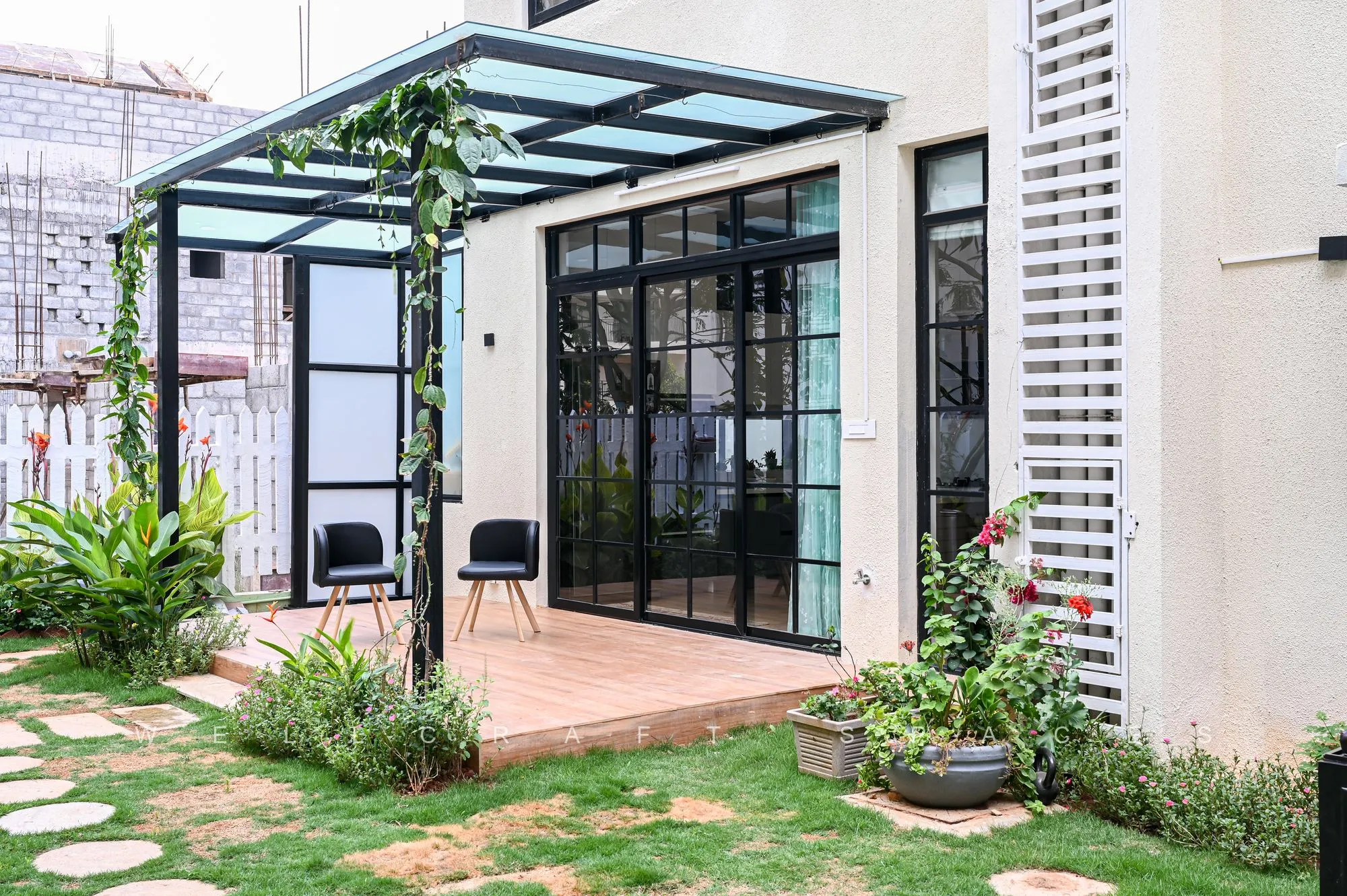 Rear courtyard with a black steel and glass pergola, potted plants and stone stepping pavers set into a clipped lawn.