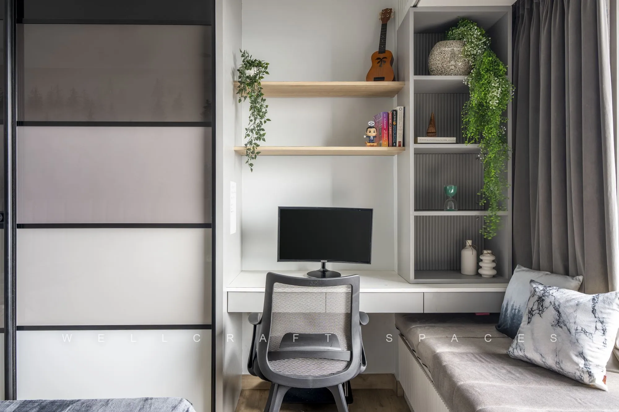Study corner with a floating white desk, open oak-lined shelving with trailing plants, a mesh task chair and a grey sliding wardrobe alongside.