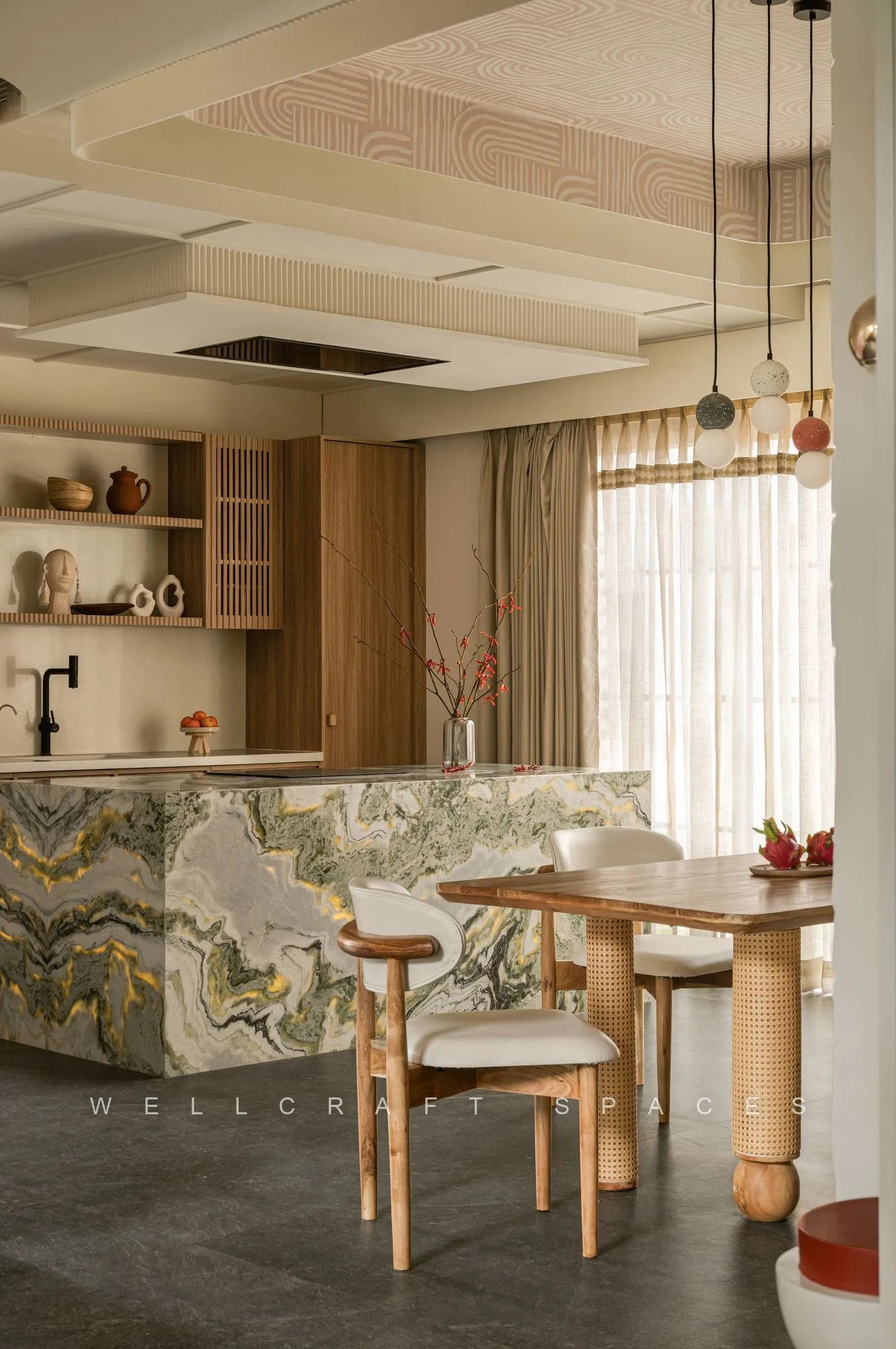 Kitchen and dining seen from above, with a green-and-gold waterfall marble island, slatted oak cabinetry and a cane-and-teak dining table lit by a cluster of glass pendant lights.